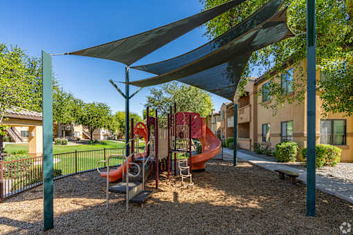 A playground with a red slide and a grey slide under a shade structure.
