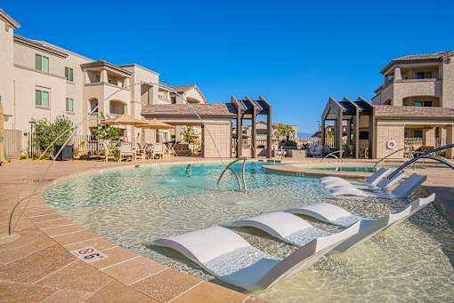 A pool with a waterfall and a white bench.