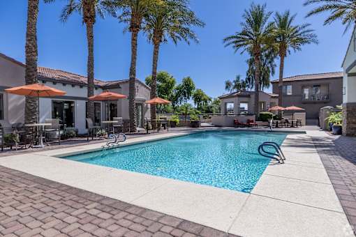 A swimming pool surrounded by palm trees and patio furniture.