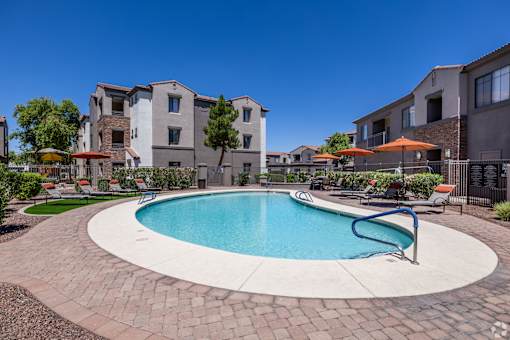 A swimming pool surrounded by a brick patio and lounge chairs.