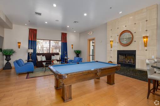 A pool table is in the middle of a room with a fireplace and a mirror.