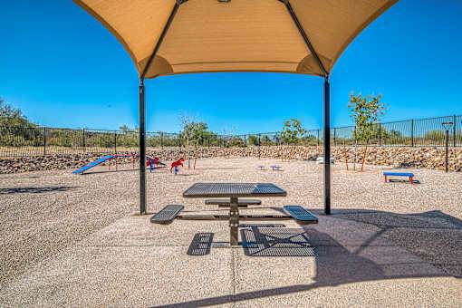 A playground with a picnic table and a canopy is set in a sunny, open area.