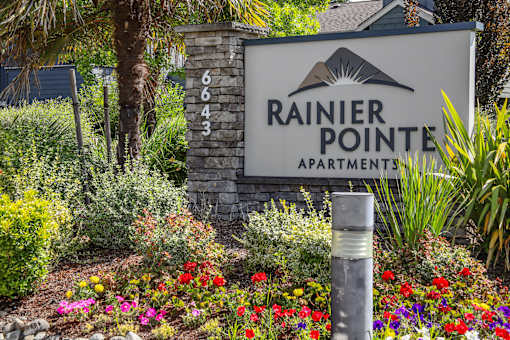 A sign for Rainier Pointe Apartments is surrounded by flowers and greenery.