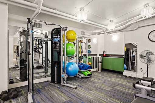 A gym with a variety of equipment including a weight machine, a bench, and a fan.