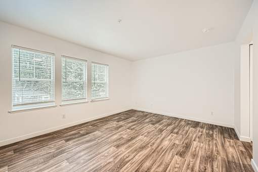 A room with wooden flooring and three windows.
