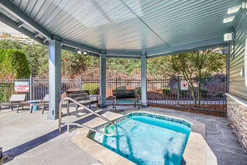 the pool is under a covered patio with chairs and a hot tub