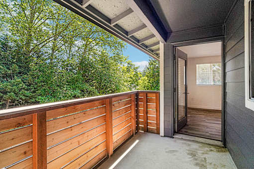 A balcony with a wooden railing and a view of trees.