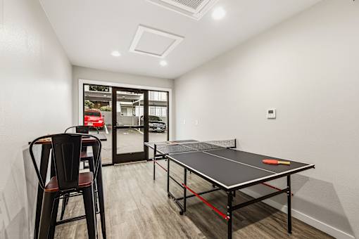 A ping pong table is in the middle of a room with a chair and a window.