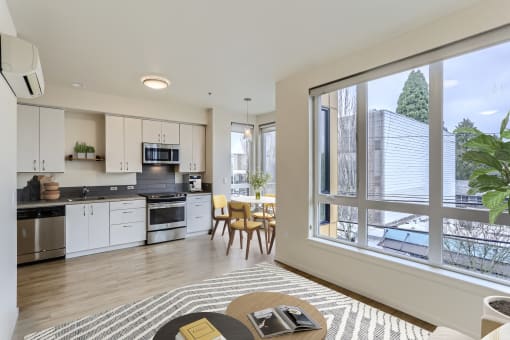 a living room with a large window and a kitchen with a table and chairs