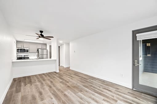 A room with a ceiling fan and a kitchen area in the background.