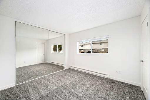 A large empty room with a grey carpet and a mirror on the wall.