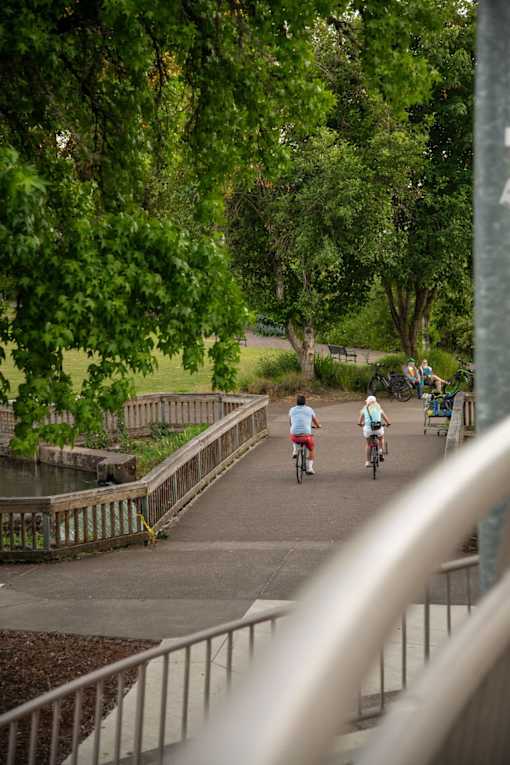 A man and a woman ride bicycles on a bridge.