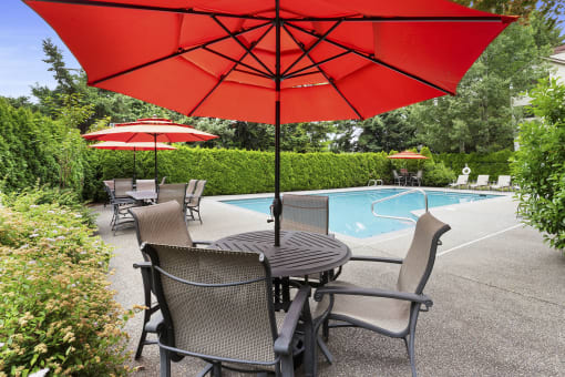 a poolside patio with a table and chairs under a red umbrella
