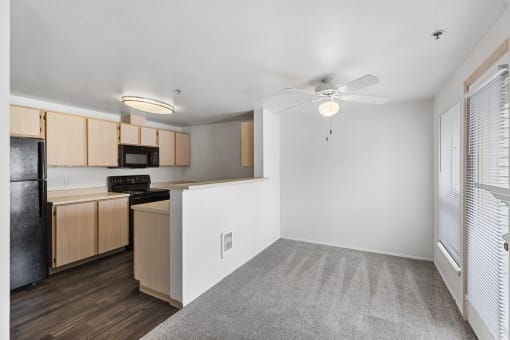 an empty living room with a kitchen and a ceiling fan
