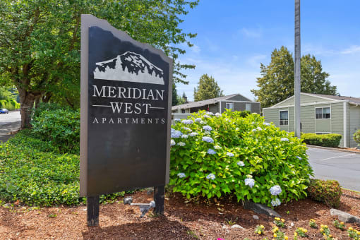 a sign for meridian west apartments in front of plants and trees