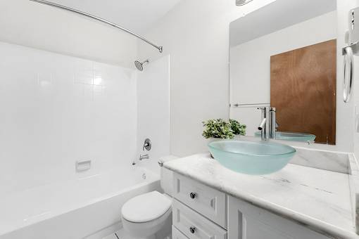 A white bathroom with a glass bowl sink and a white toilet.