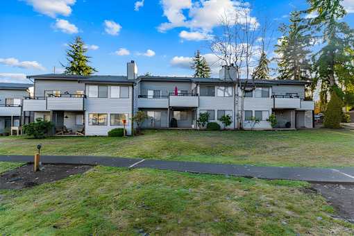 Apartment complex with a grassy area in front and trees in the background.