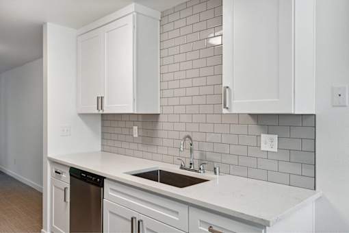 A kitchen with white cabinets and a grey tile backsplash.