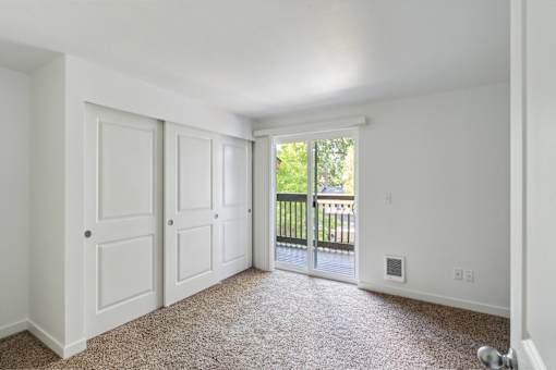 A room with white walls and a carpeted floor with a sliding glass door leading to a balcony.