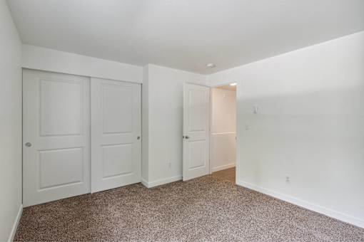 A room with white walls and carpeted floor with three doors.
