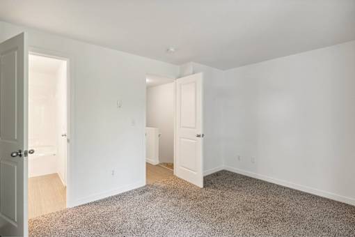 A room with white walls and a carpeted floor with two doors.