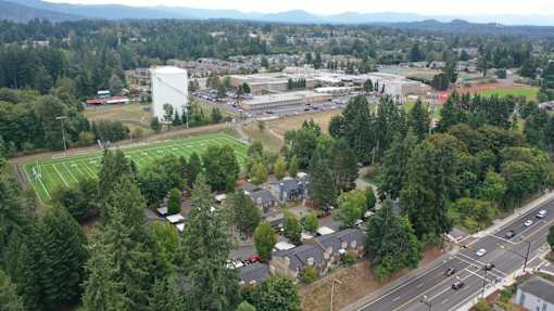 A view of a town with a large white building in the middle of a green field.