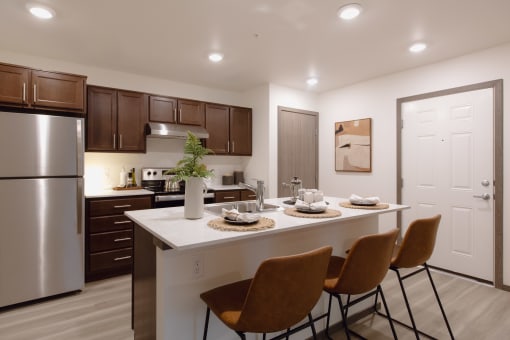 a kitchen with a large island with four chairs and a stainless steel refrigerator