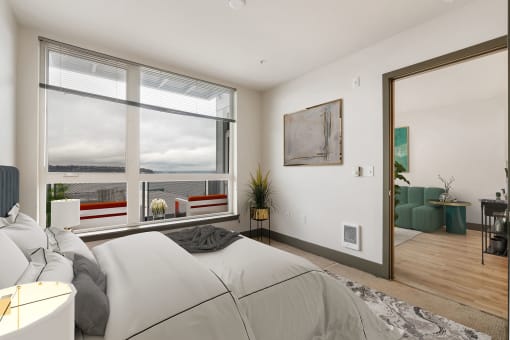 a bedroom with a large window and a door that leads to a living room