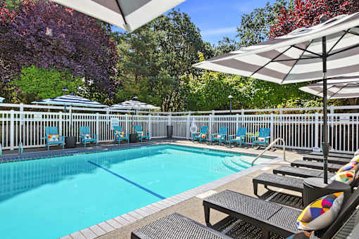 A pool surrounded by trees and chairs.