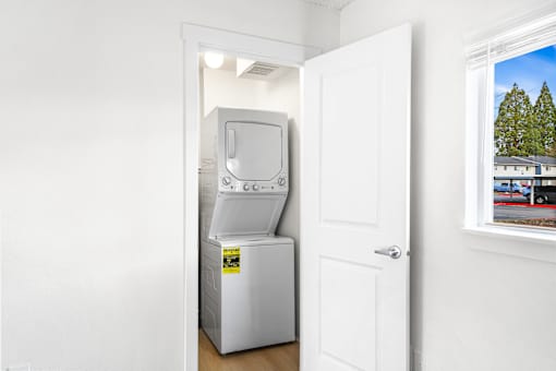 A white door is open to a room with a fridge and a window showing a tree.
