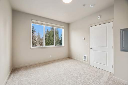A room with a white door and a window overlooking a forest.