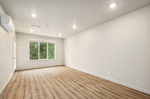 A room with wooden flooring and a window showing greenery outside.