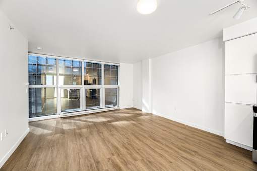 A room with wooden flooring and a large window with a view of a cityscape.