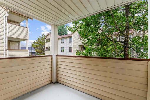 a covered porch with a view of trees and apartment buildings