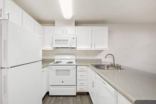 A white kitchen with a refrigerator, microwave, oven, and sink.