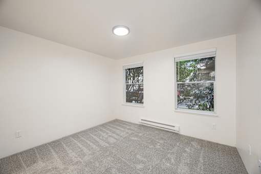 A room with a carpeted floor and two windows.