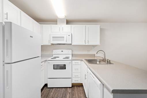 A white kitchen with a refrigerator, microwave, oven, and sink.