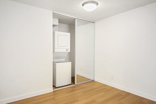 A white refrigerator is in a room with a white wall and wooden floor.