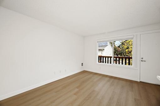 A room with a white door and a window showing a balcony with a white house and trees in the background.