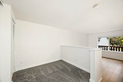 A room with a carpeted floor and a window with a view of a balcony.