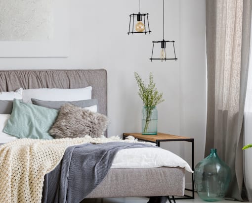 A grey bed with a grey blanket and pillows with a white pillowcase.