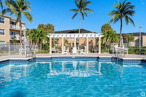 A pool with a white pergola and palm trees in the background.