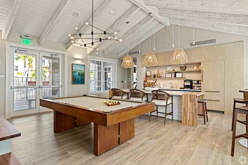 A billiard table is in the middle of a room with a kitchen area in the background.