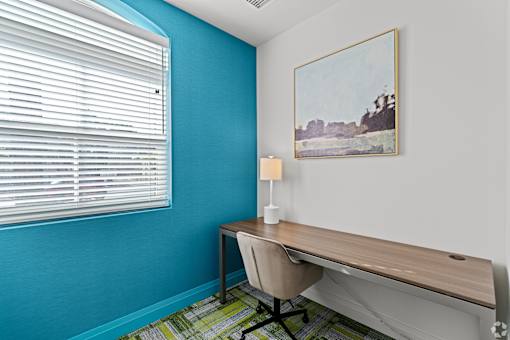 A room with a desk, chair, and a painting on the wall.