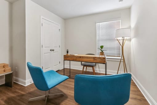 a living room with two blue chairs and a desk and a window