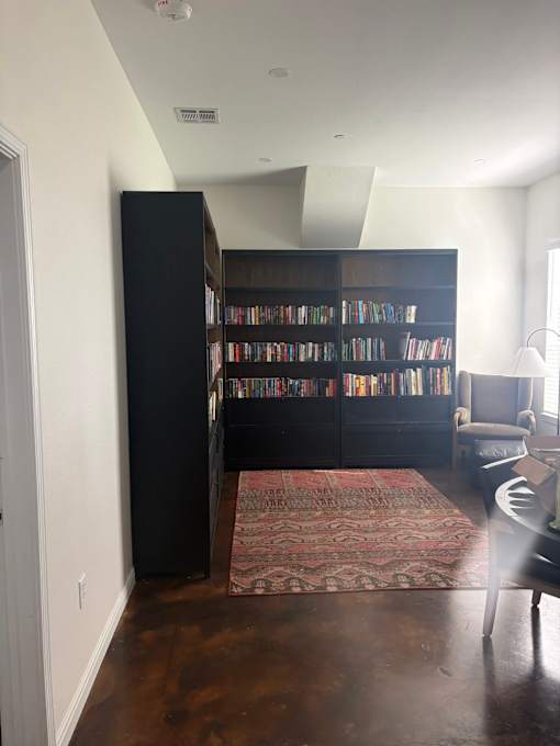 A room with a bookshelf filled with books and a rug on the floor.