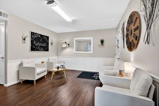 A living room with white furniture and a large clock on the wall.