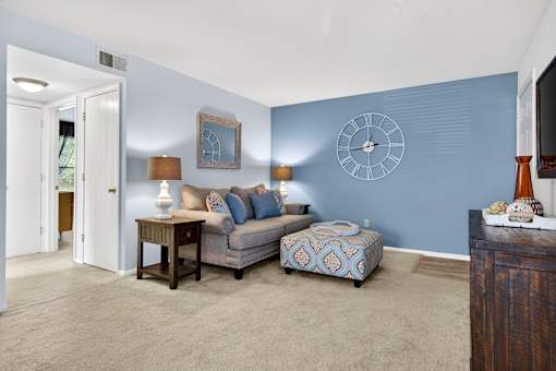 A living room with a grey couch, a small table, and a clock on the wall.
