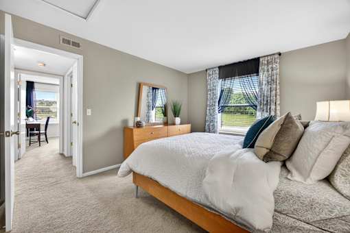 A bedroom with a large bed and a view of the backyard through the window.