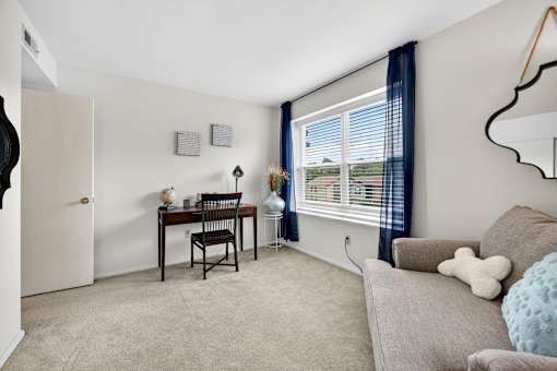 A room with a desk, chair, and window with blinds.